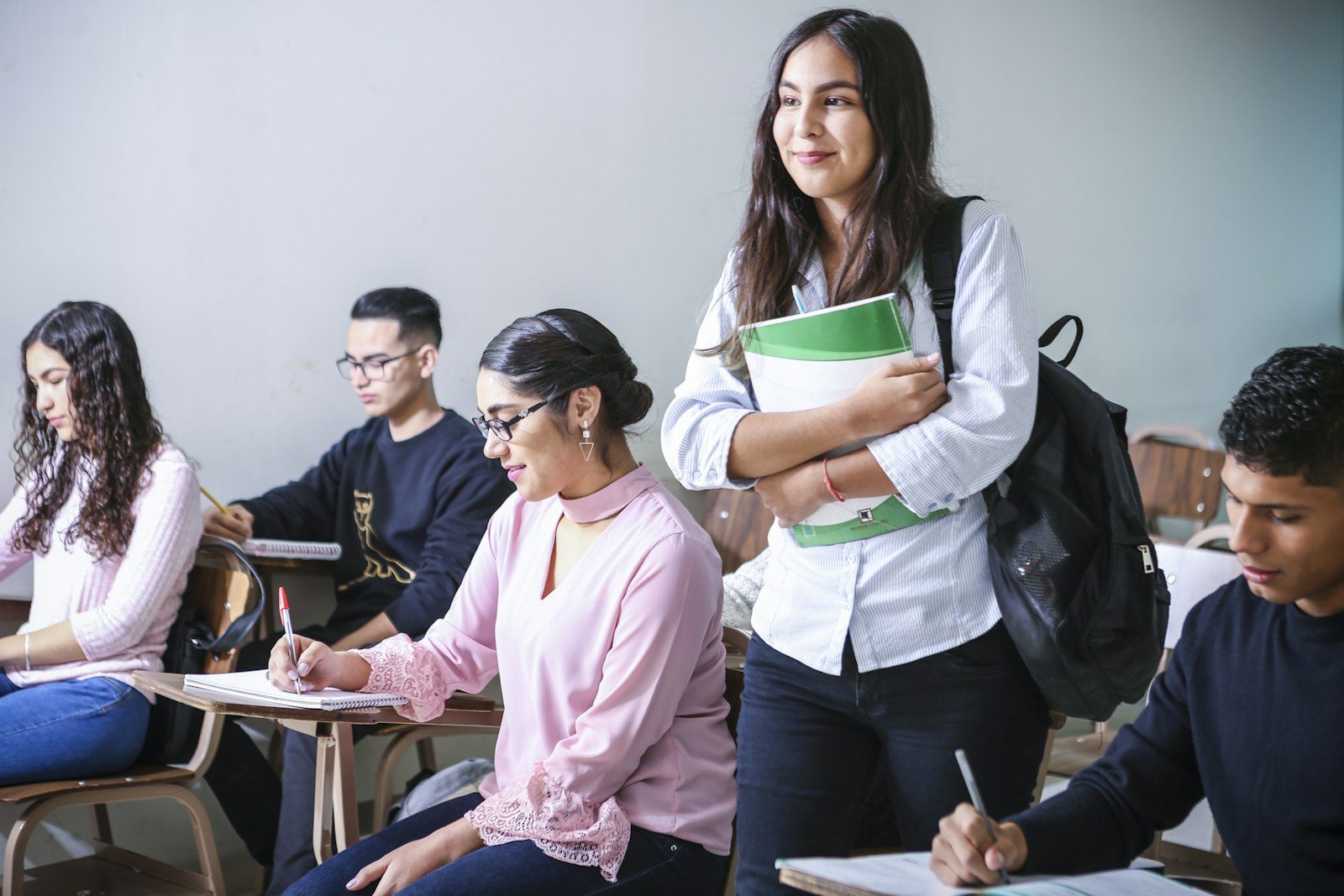 A student carrying books through a busy classroom